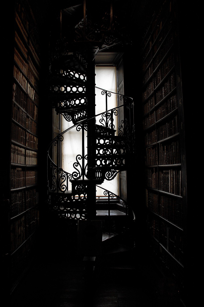 Photograph of a backlit spiral staircase between library stacks.
